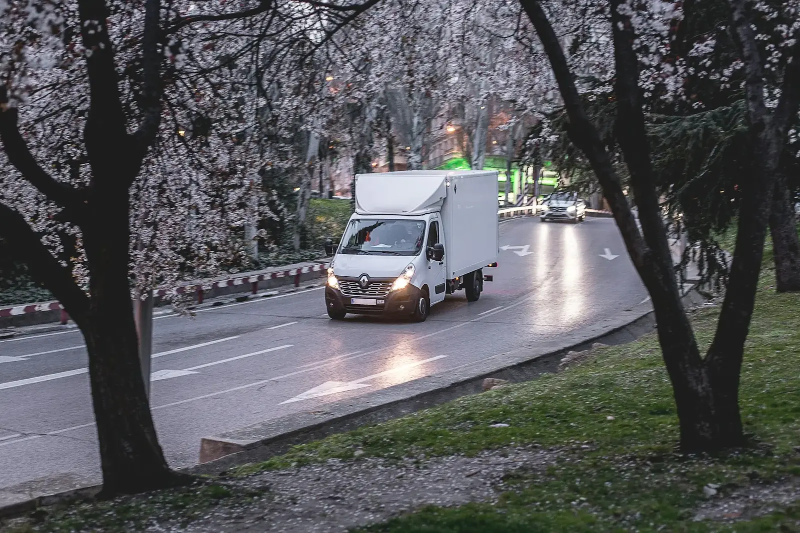 White box truck driving on a tree-lined road